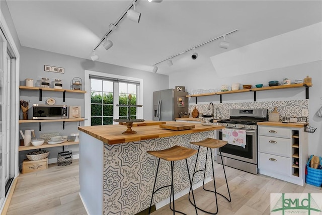 kitchen with butcher block counters, track lighting, stainless steel appliances, and a breakfast bar