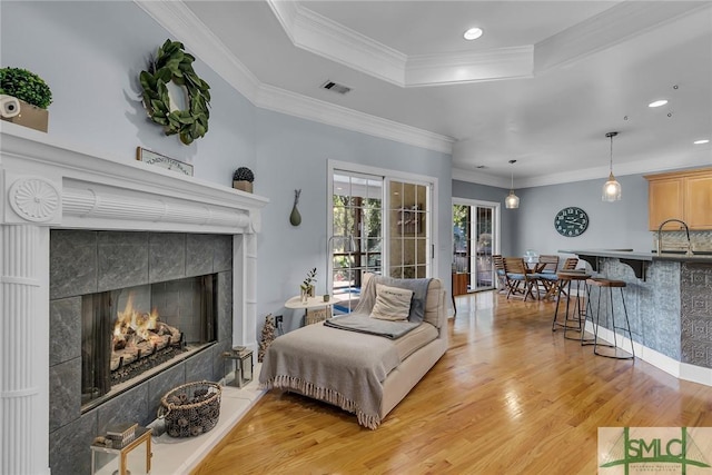 living room featuring a tiled fireplace, hardwood / wood-style flooring, ornamental molding, and a raised ceiling