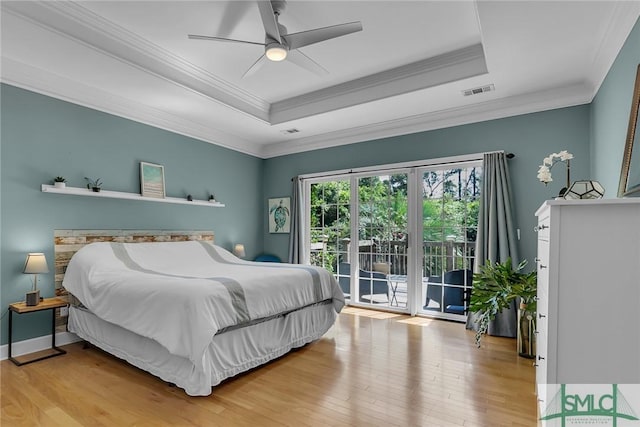 bedroom with crown molding, a tray ceiling, light hardwood / wood-style flooring, and access to outside