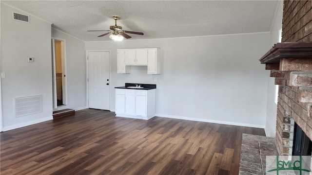 unfurnished living room with sink, a brick fireplace, a textured ceiling, dark hardwood / wood-style flooring, and ceiling fan