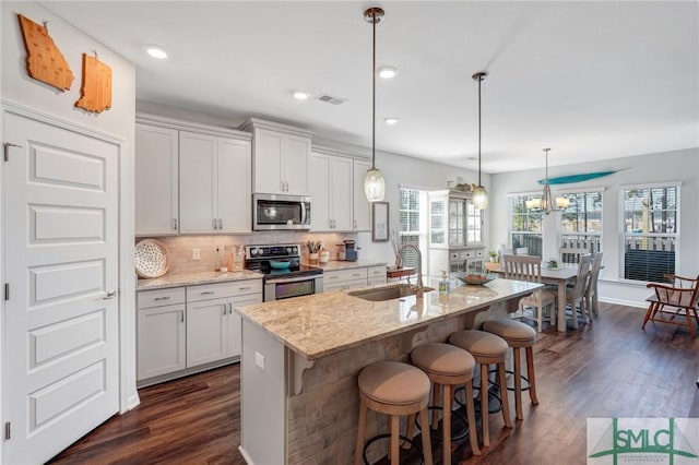 kitchen with pendant lighting, sink, appliances with stainless steel finishes, light stone counters, and an island with sink