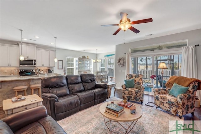 living room featuring ceiling fan with notable chandelier and light hardwood / wood-style flooring