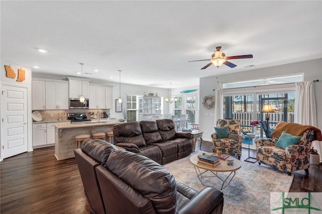 living room with plenty of natural light, dark hardwood / wood-style floors, ceiling fan with notable chandelier, and sink