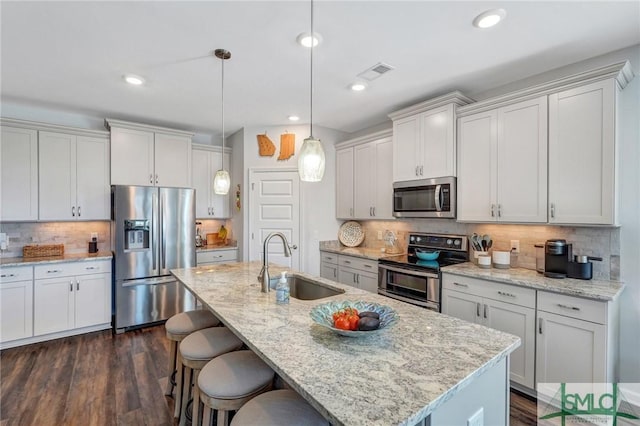 kitchen with an island with sink, appliances with stainless steel finishes, decorative light fixtures, and sink