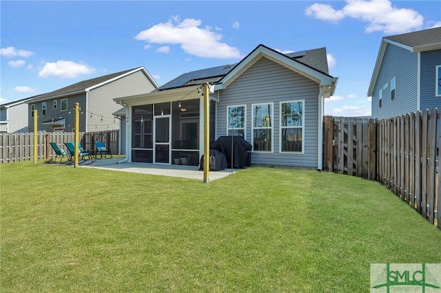 back of property with a yard, a patio area, a sunroom, and solar panels