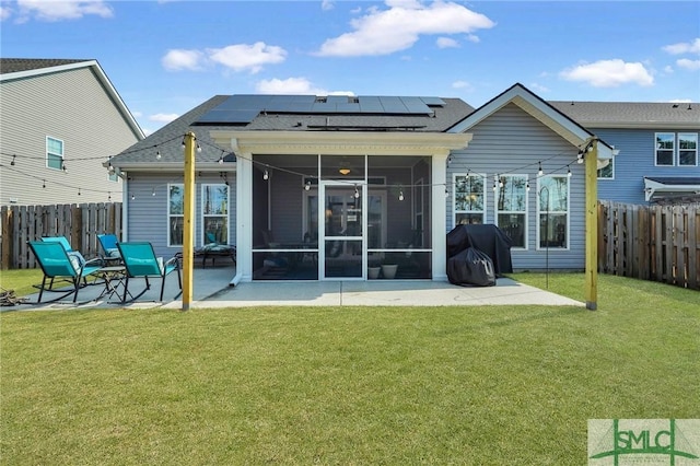 rear view of property featuring a lawn, a patio area, a sunroom, and solar panels