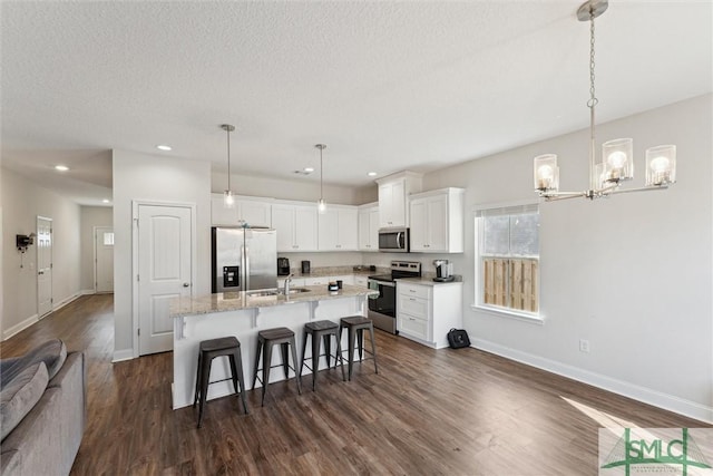 kitchen with appliances with stainless steel finishes, pendant lighting, light stone countertops, a kitchen island with sink, and white cabinets