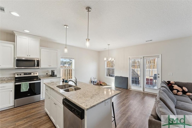 kitchen with sink, white cabinetry, decorative light fixtures, stainless steel appliances, and a kitchen island with sink