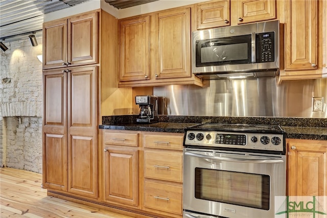 kitchen with light wood-style floors, appliances with stainless steel finishes, and dark stone countertops