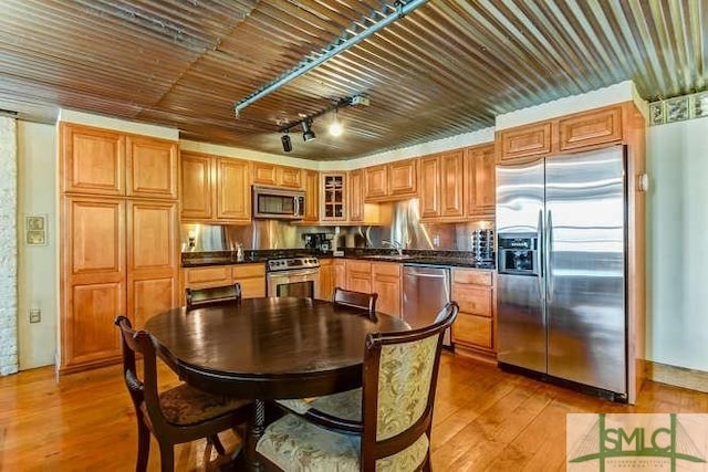 kitchen featuring dark countertops, hardwood / wood-style flooring, glass insert cabinets, brown cabinets, and stainless steel appliances