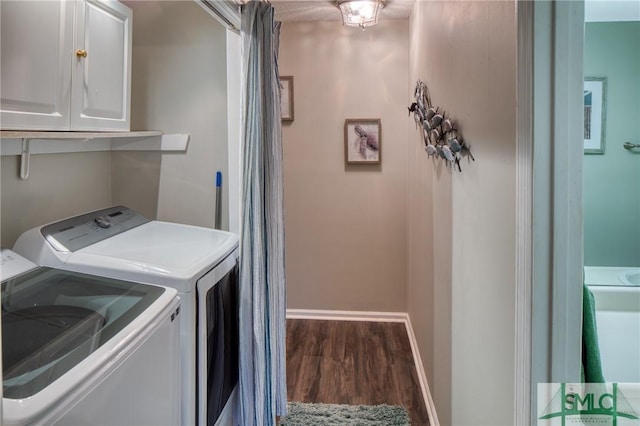 laundry area with dark wood-type flooring, washer and clothes dryer, and cabinets