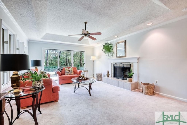 carpeted living room with a tiled fireplace, ornamental molding, a textured ceiling, and a tray ceiling