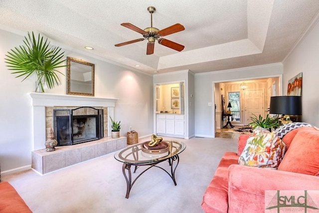 living room featuring light carpet, a textured ceiling, ornamental molding, a raised ceiling, and a tile fireplace