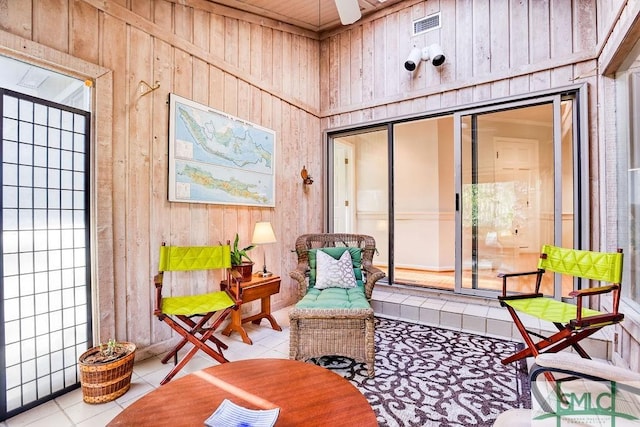 sitting room with light tile patterned floors, ceiling fan, and wood walls