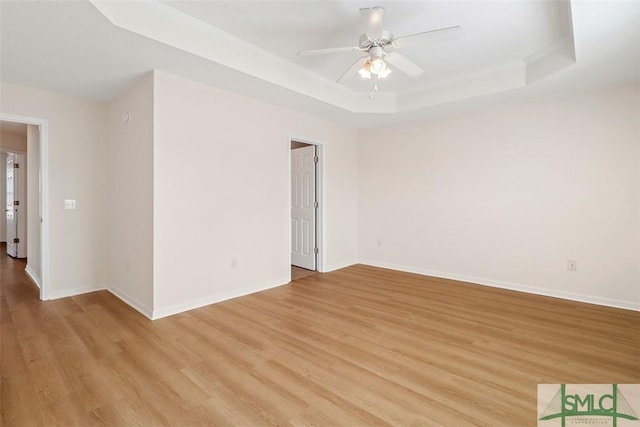 empty room with a tray ceiling, light hardwood / wood-style floors, and ceiling fan