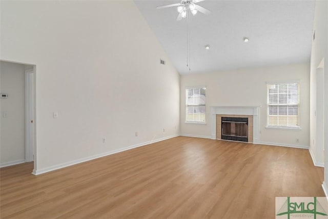 unfurnished living room featuring high vaulted ceiling, light hardwood / wood-style flooring, a tile fireplace, and ceiling fan