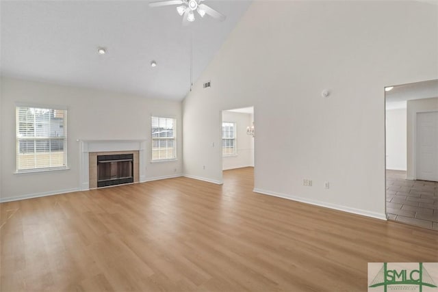 unfurnished living room featuring ceiling fan, high vaulted ceiling, light hardwood / wood-style floors, and a tile fireplace