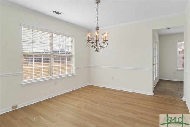 spare room featuring wood-type flooring, plenty of natural light, and an inviting chandelier