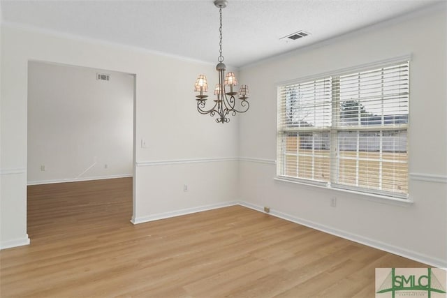 spare room with wood-type flooring, ornamental molding, a textured ceiling, and a chandelier