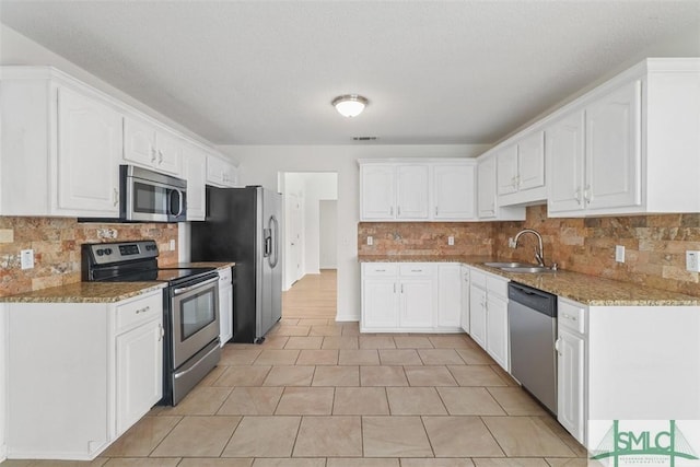 kitchen with stainless steel appliances, white cabinetry, sink, and light stone counters