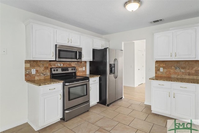 kitchen featuring light tile patterned flooring, appliances with stainless steel finishes, white cabinetry, backsplash, and dark stone counters