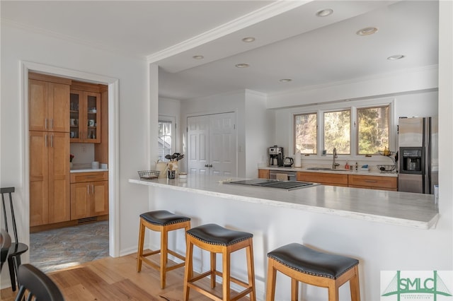 kitchen featuring sink, crown molding, a kitchen breakfast bar, kitchen peninsula, and stainless steel refrigerator with ice dispenser