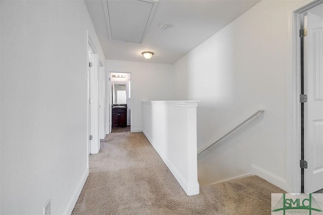 corridor featuring attic access, baseboards, light colored carpet, and an upstairs landing