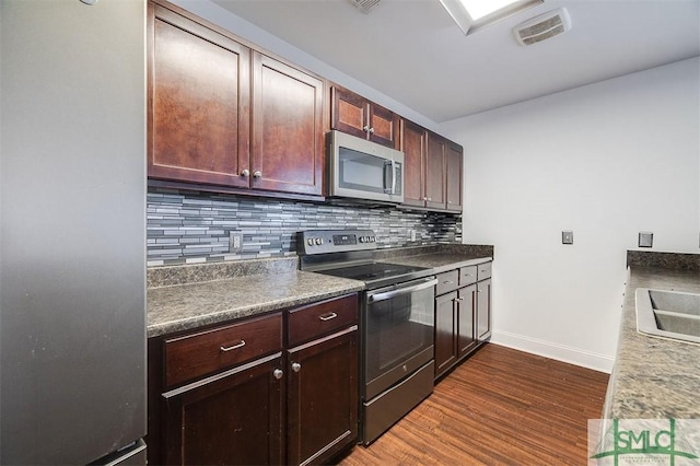 kitchen with stainless steel appliances, dark wood-type flooring, visible vents, tasteful backsplash, and dark countertops