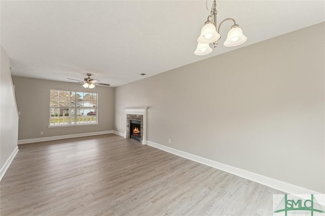 unfurnished living room with a stone fireplace, ceiling fan with notable chandelier, and light hardwood / wood-style flooring