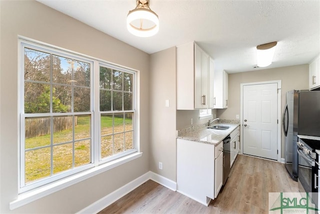 kitchen featuring stainless steel appliances, light stone countertops, white cabinets, and light hardwood / wood-style floors