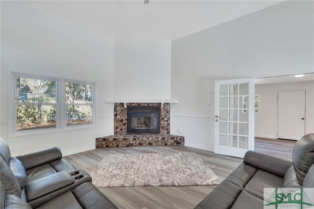 living room with french doors, a stone fireplace, light hardwood / wood-style flooring, and a high ceiling