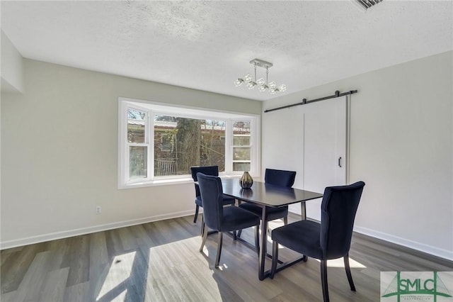 dining room featuring dark hardwood / wood-style flooring, a barn door, a textured ceiling, and an inviting chandelier