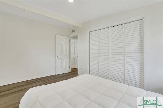 bedroom featuring dark hardwood / wood-style floors, beam ceiling, and a closet