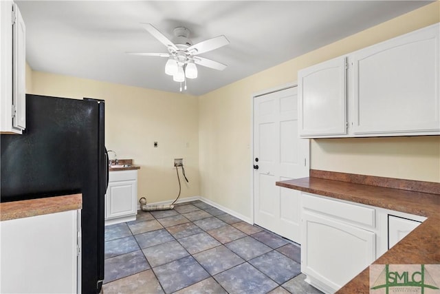 kitchen with a ceiling fan, dark countertops, white cabinetry, freestanding refrigerator, and baseboards