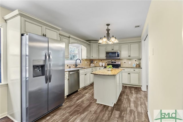 kitchen with sink, light stone counters, decorative light fixtures, a center island, and stainless steel appliances