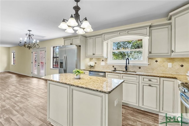 kitchen with a sink, backsplash, a kitchen island, appliances with stainless steel finishes, and a chandelier