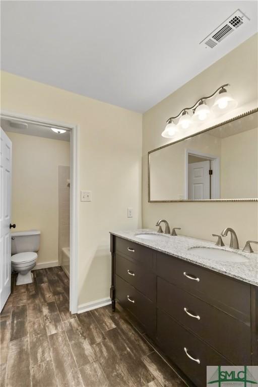 full bathroom featuring washtub / shower combination, wood-type flooring, toilet, and vanity