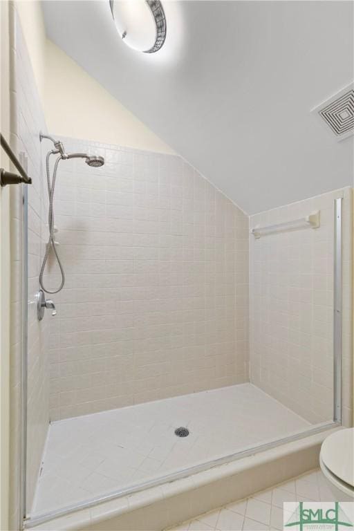 bathroom with a tile shower, tile patterned flooring, lofted ceiling, and toilet