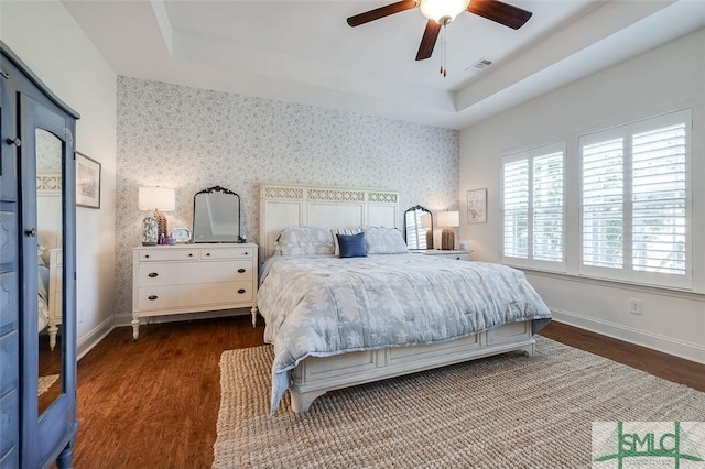 bedroom with dark wood-type flooring, ceiling fan, and a raised ceiling