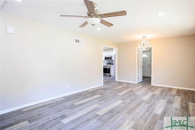 unfurnished living room with ceiling fan with notable chandelier and light hardwood / wood-style floors