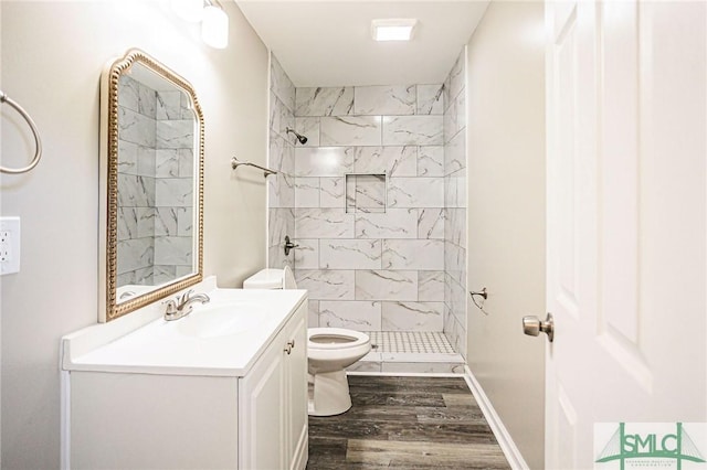 bathroom featuring hardwood / wood-style flooring, vanity, a tile shower, and toilet