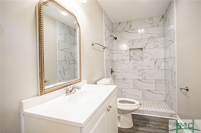 bathroom featuring a tile shower, vanity, hardwood / wood-style flooring, and toilet