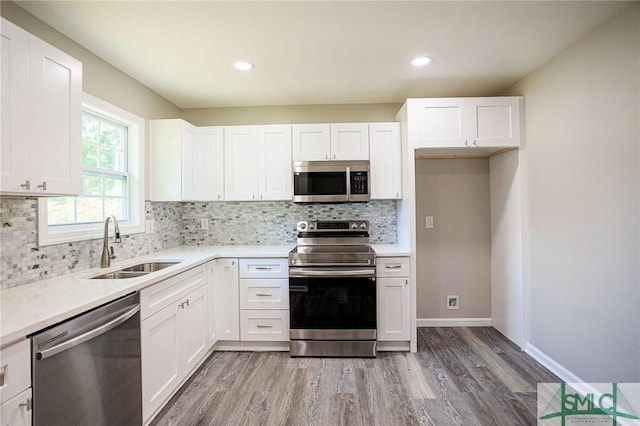 kitchen with sink, white cabinetry, hardwood / wood-style floors, backsplash, and stainless steel appliances