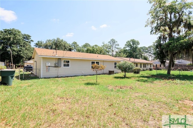 rear view of house featuring central AC unit and a lawn