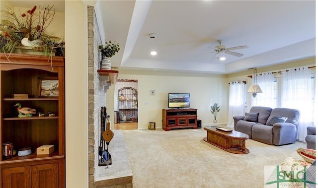 carpeted living room with ceiling fan, a raised ceiling, and a brick fireplace