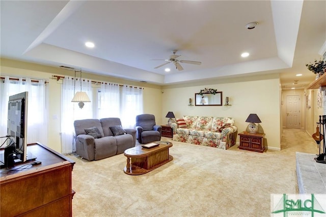 carpeted living room with ceiling fan and a tray ceiling