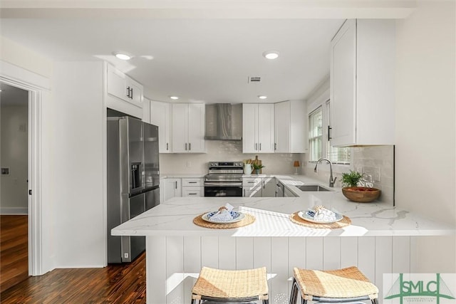 kitchen with a sink, wall chimney exhaust hood, a peninsula, appliances with stainless steel finishes, and dark wood-type flooring