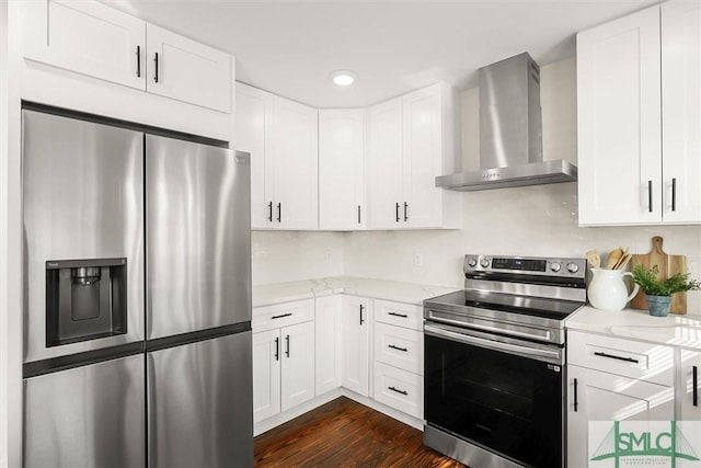 kitchen with dark wood-type flooring, appliances with stainless steel finishes, white cabinetry, light stone countertops, and wall chimney exhaust hood