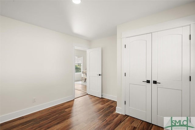 unfurnished bedroom with baseboards, dark wood-type flooring, and a closet