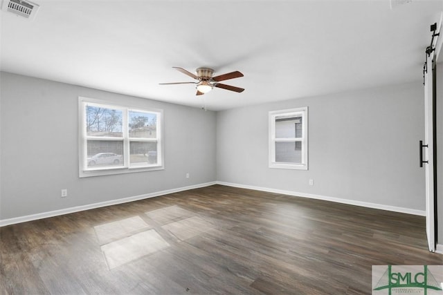 empty room with dark hardwood / wood-style flooring, a barn door, and ceiling fan